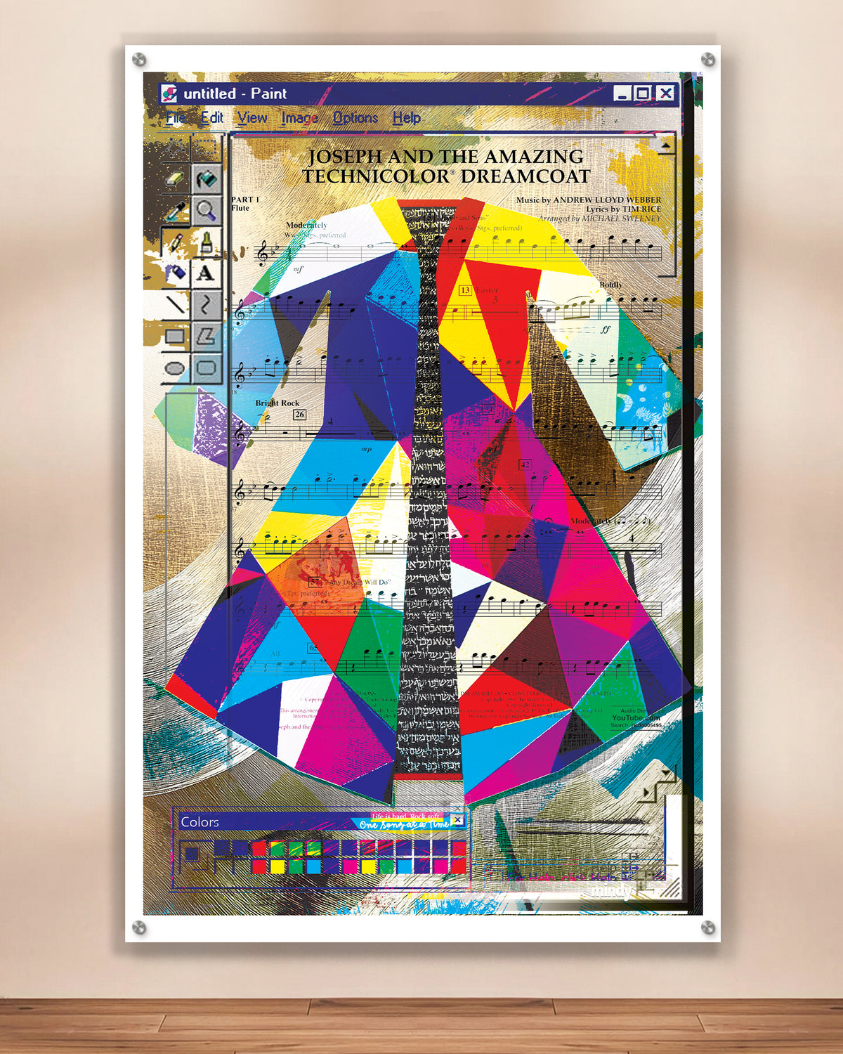 A metal art print depicting Jospeh and The Amazing Technicolor Dreamcoat design over sheet music, displayed against a beige wall above a wooden floor.